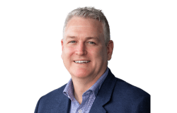 Headshot of James Lye. Portrait of a middle-aged man with short, silver hair, smiling at the camera. He is wearing a blue blazer over a checkered button-up shirt.