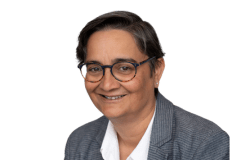 Headshot of Nadine Bartholomeusz-Raymond. Woman with short dark hair, dark skin, glasses, wearing a grey jacket and white shirt.