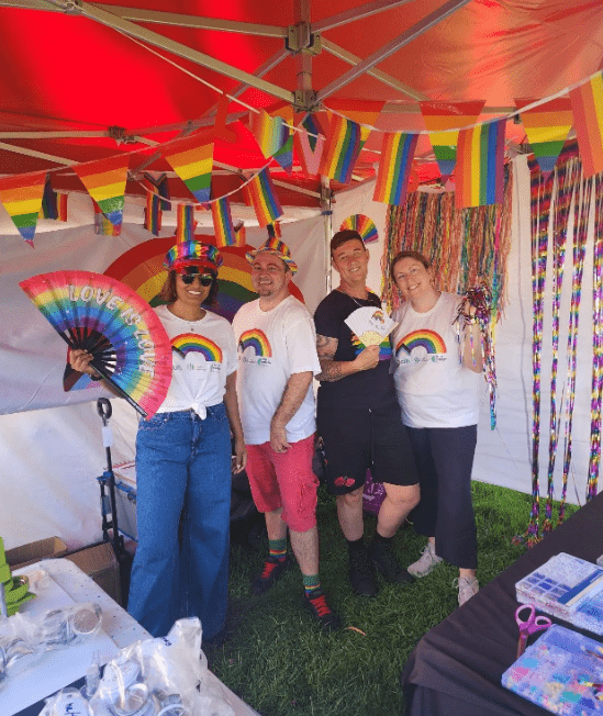 4 people wearing mcm rainbow shirts in a marque decorated with rainbow flags