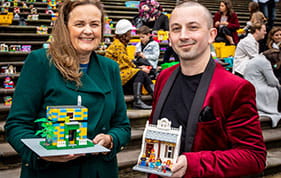 Female and male standing on steps of Parliment House with Lego Houses