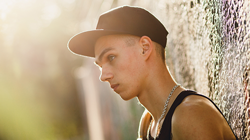 Male teenager wearing baseball cap leaning against a wall