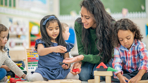 Teacher plays with three children on the floor at a childcare setting