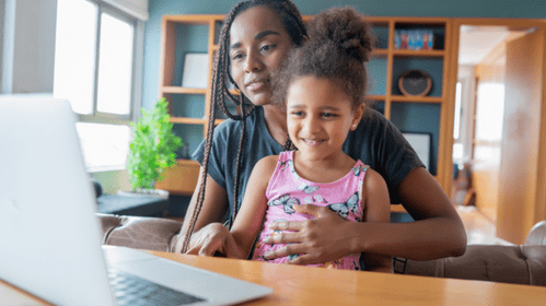 A young girl sits on her Mum's knee on front of a laptop