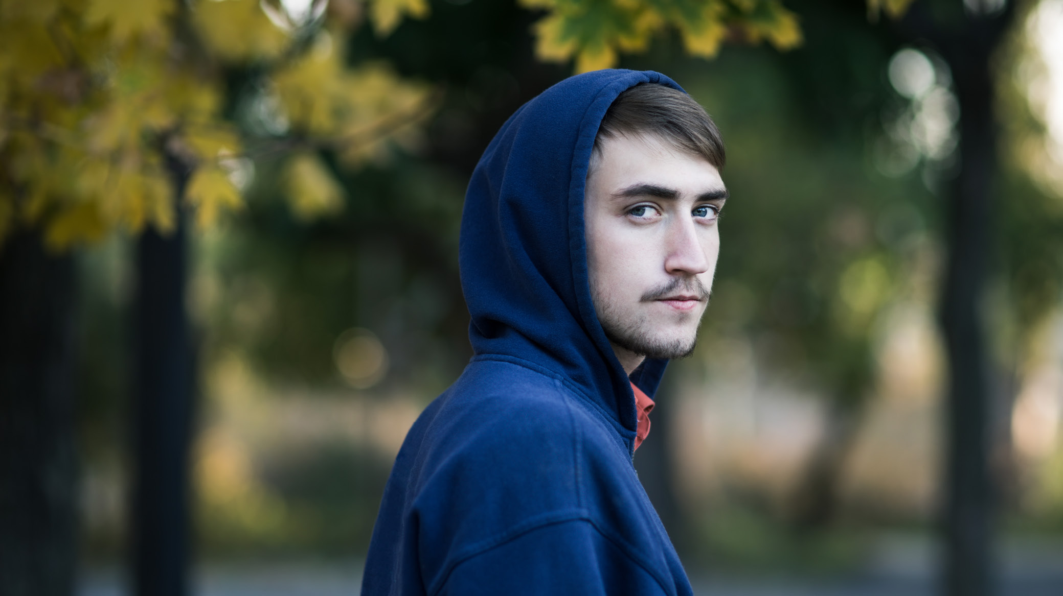 Young man wearing a blue hoodie with brown hair looking at the camera