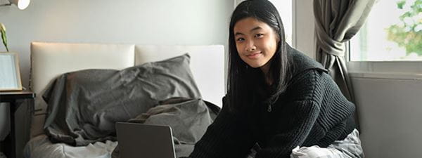 A young female teenager sitting on her bed with a laptop