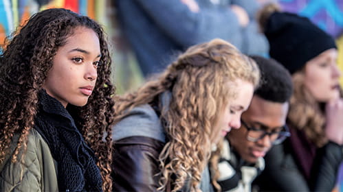 Teenagers wearing winter jackets sit on the curb in a line