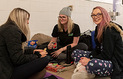 Group of three girls at Sleep At The G sitting on the floor playing cards