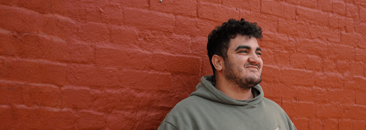 young male wearing a grey hoodie standing in front of a red wall. looking off to the right