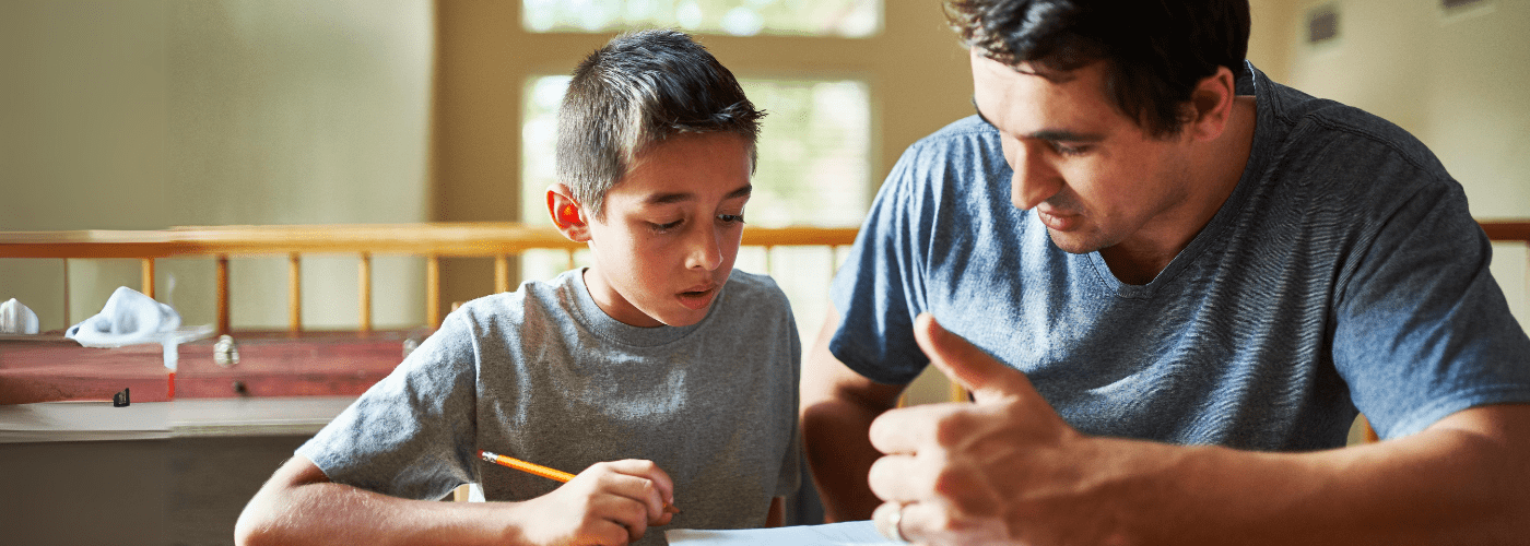 son and father sitting at table while father explains homework