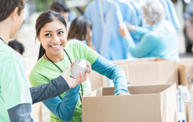 Teenage girl wearing a green t-shirt packs a box with cans of food