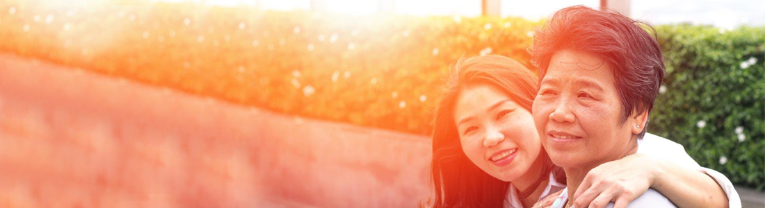 Two Asian ladies, one younger and one older sitting together. The young lady has her arm around the older lady's shoulder