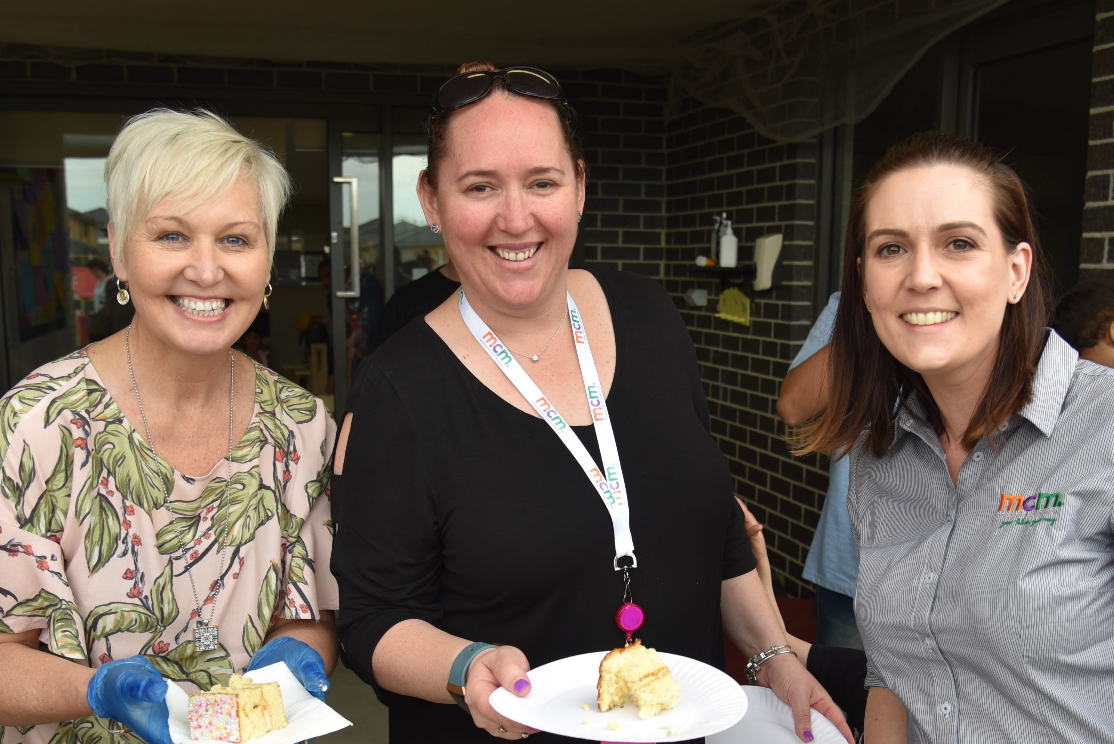 Three female MCM staff smiling at the camera while they serve birthday cake