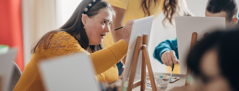 woman in a yellow jumper with a disability painting a canvas