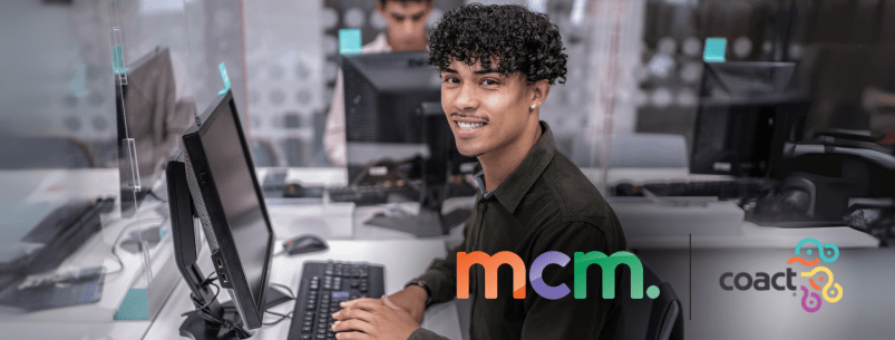 young man sitting at a computer facing the camera and smiling. The MCM and Coact logos are in the bottom right corner.
