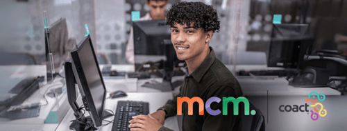 young man sitting at a computer facing the camera and smiling. The MCM and Coact logos are in the bottom right corner.
