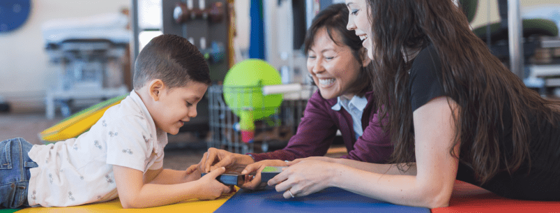 boy playing on floor with therapist and parent