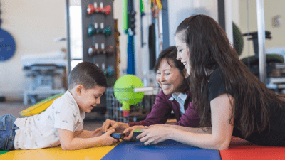 boy playing on floor with therapist and parent