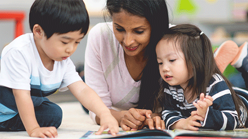 Two children reading on the floor with an educator
