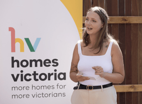 young woman speaking in front of homes victoria banner
