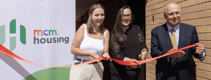 3 people holding and cutting a ribbon in front of a building