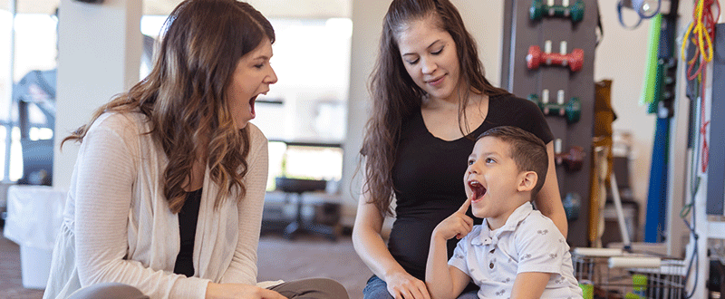 Speech pathologist sits on the floor with a small boy and his Mum