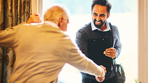 Older man greets younger man at the door