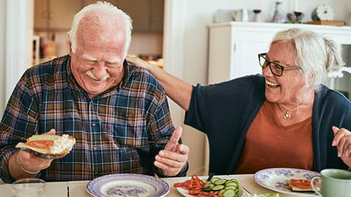 Two adults laughing and eating dinner together as they sis side by side