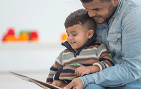 A Dad sits with his son on his lap as they read a book together