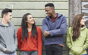 Group of four young people, make and female, stand up against a wall