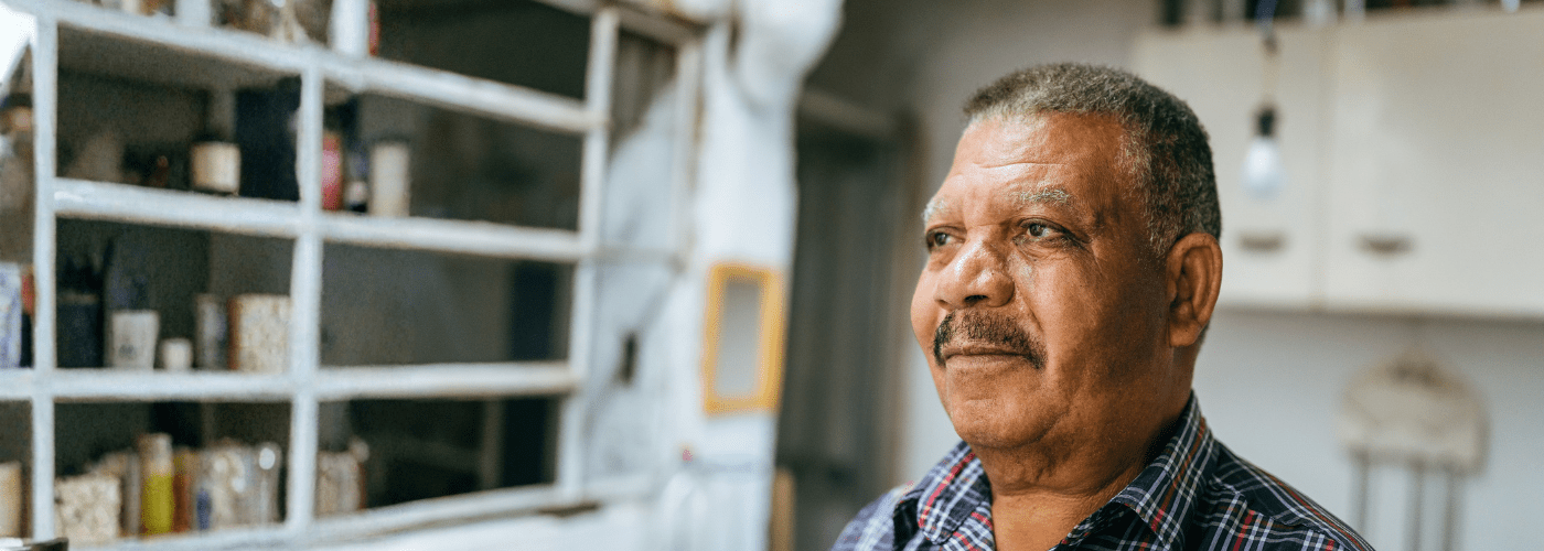 Older man standing in a kitchen looking thoughtful