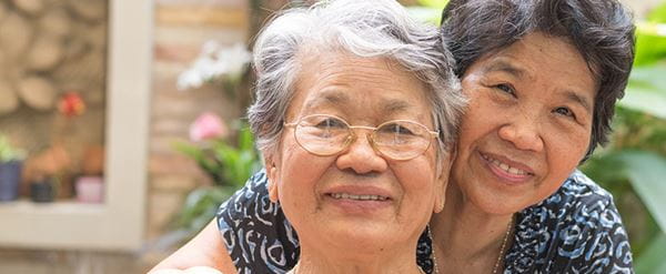 Two elderly Asian women, one with glasses, sit together smiling