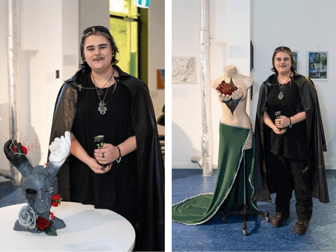 Ritter Jäger stands next their artworks, one is a sculpture of  a mask with two hands, the other is a mannequin draped in a green skirt with hands holding out a realistic looking heart.