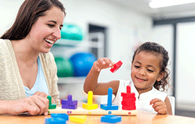 A young girl plays with blocks beside her female educator