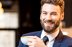 Man in navy suit smiling and holding a cup of coffee.