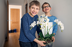 Two young boys smiling at the camera holding a green plant and flower
