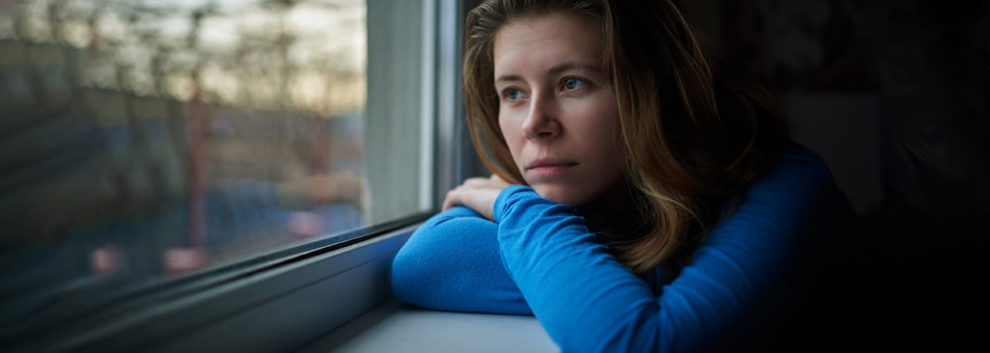 Teenage girl wearing blue top folds her arms while looking out a window